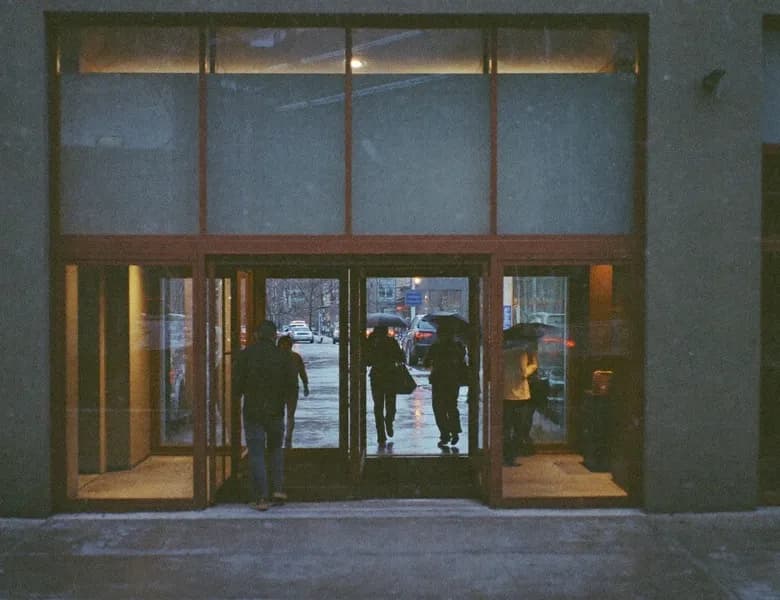 People walking through the glass doors of an office building on a rainy day