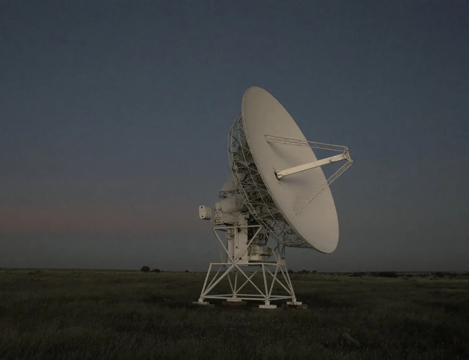 A radio telescope dish standing in an open field at dusk