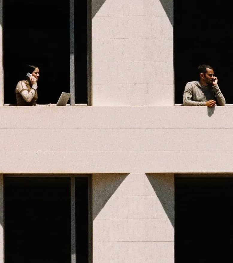 People working at desks, seen through the windows of a pale building