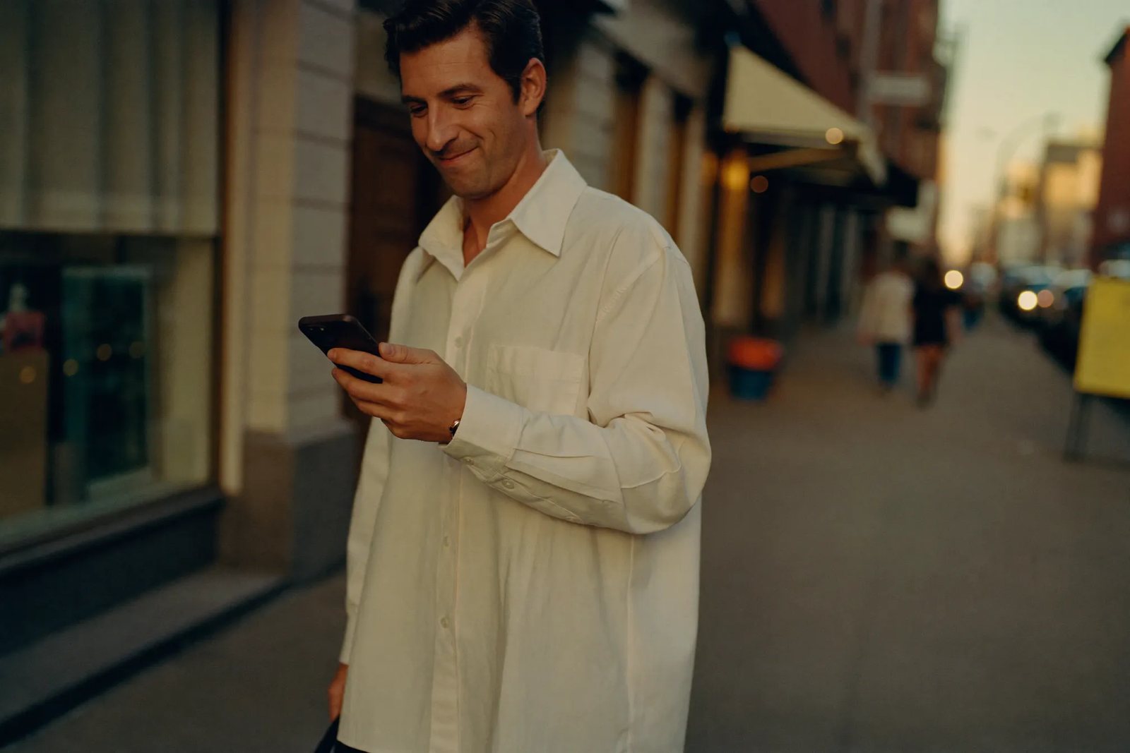 A customer reading and replying to a text message while walking down a city street at dusk