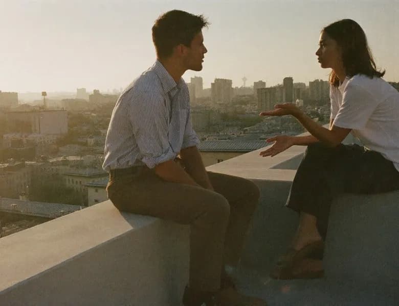 Two colleagues talking on a rooftop above a city at sunset
