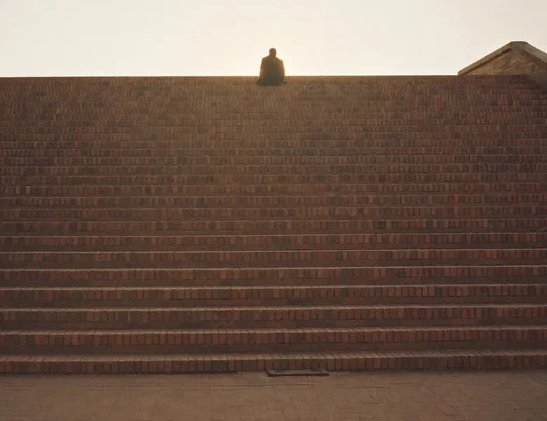 A lone figure sitting on top of a brick wall against an evening sky