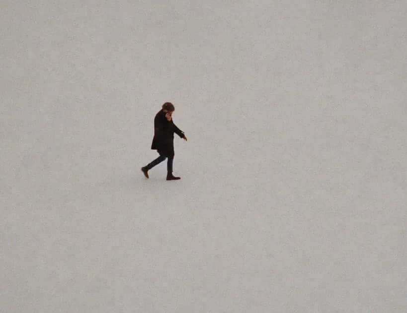 A single person walking across a wide, empty pale space
