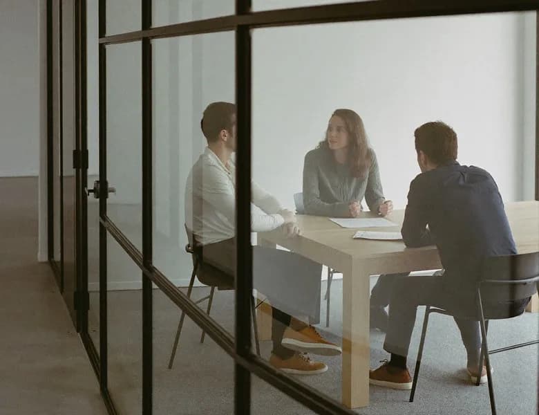 Three people meeting at a table behind a glass office wall