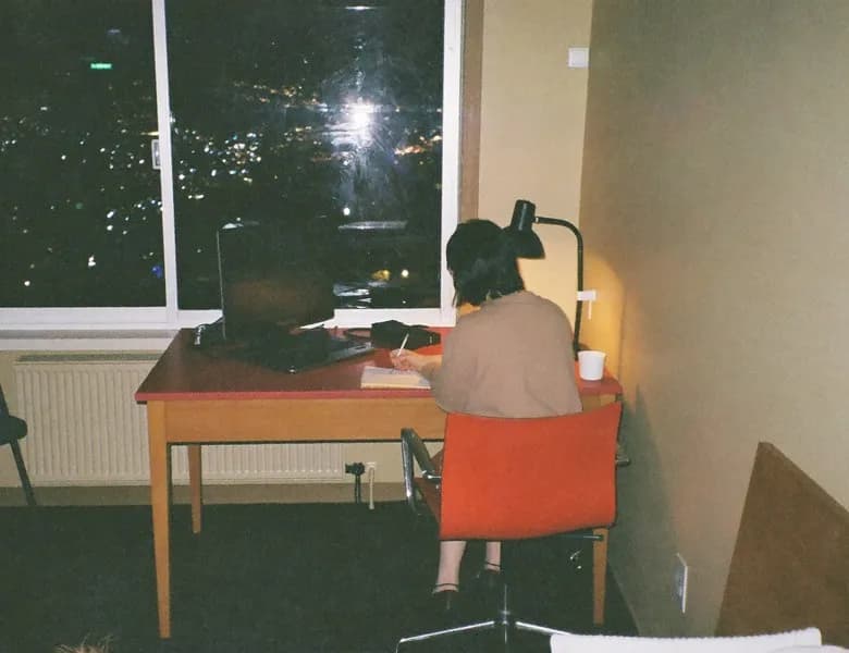 A person working at a desk by a window at night, with city lights outside
