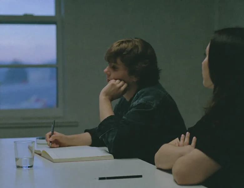 Two people listening and taking notes at a table by a window