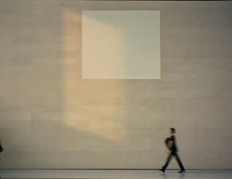 Two people walking across a large, sunlit stone hall
